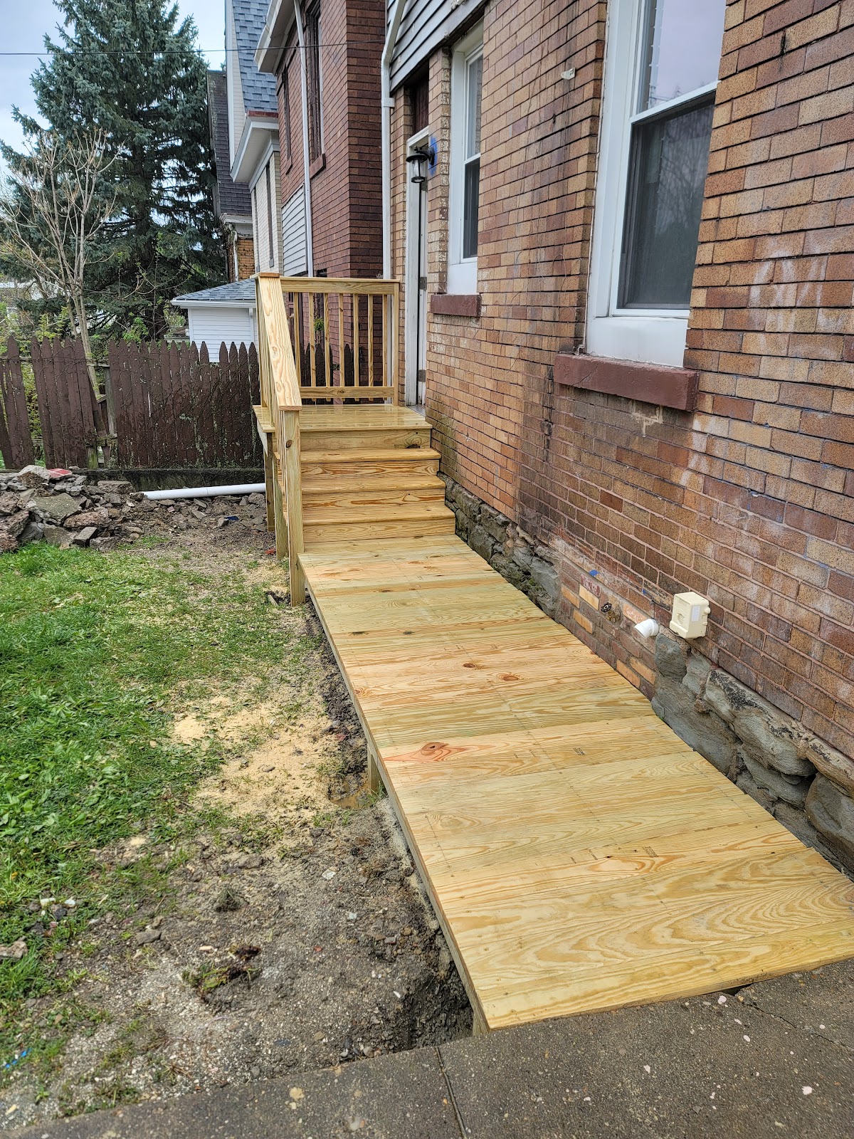 Custom-built wooden accessibility ramp and steps leading to a brick rowhouse's back door